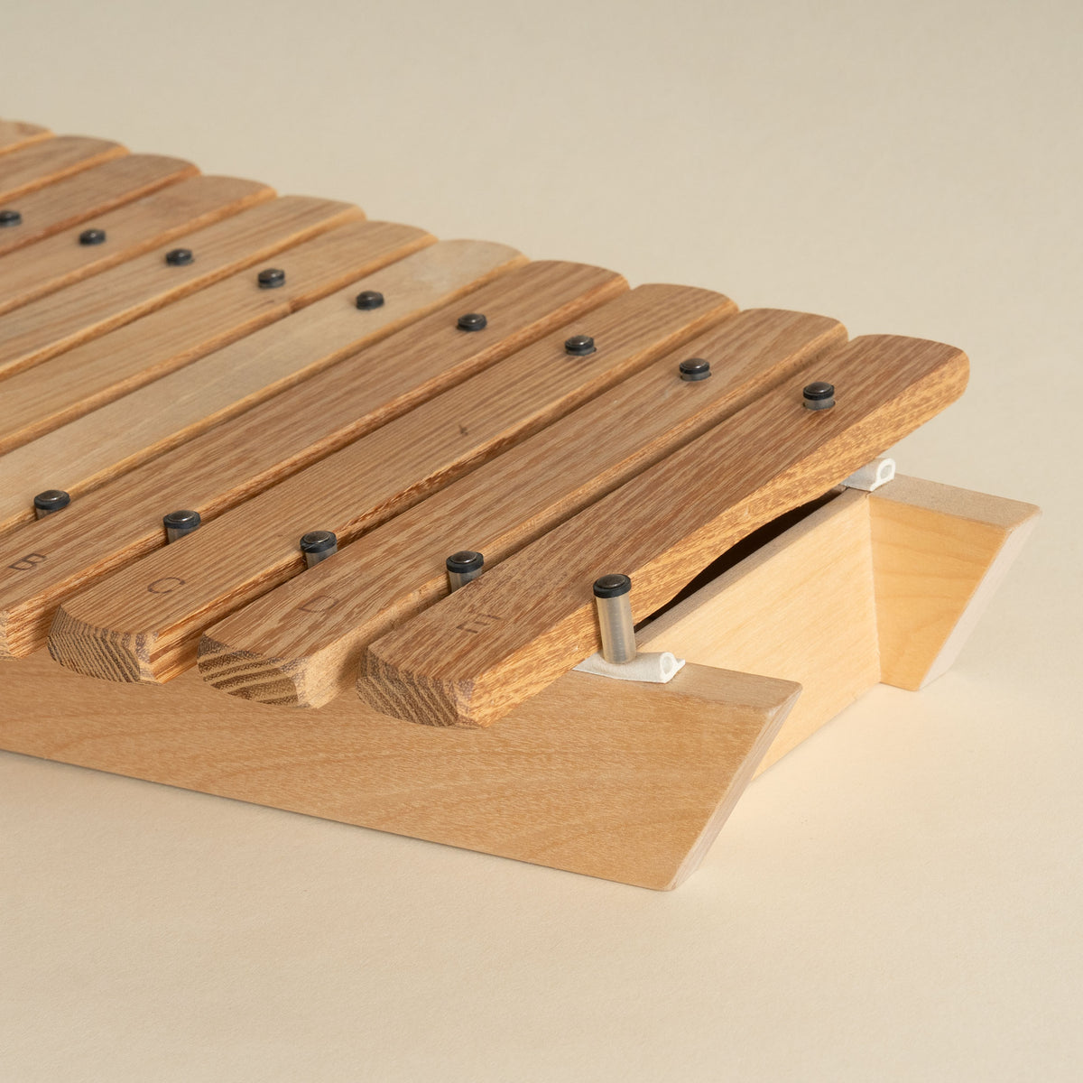 A close-up of a wooden xylophone with light natural wood bars and a matching wooden base, photographed on a plain warm beige background.