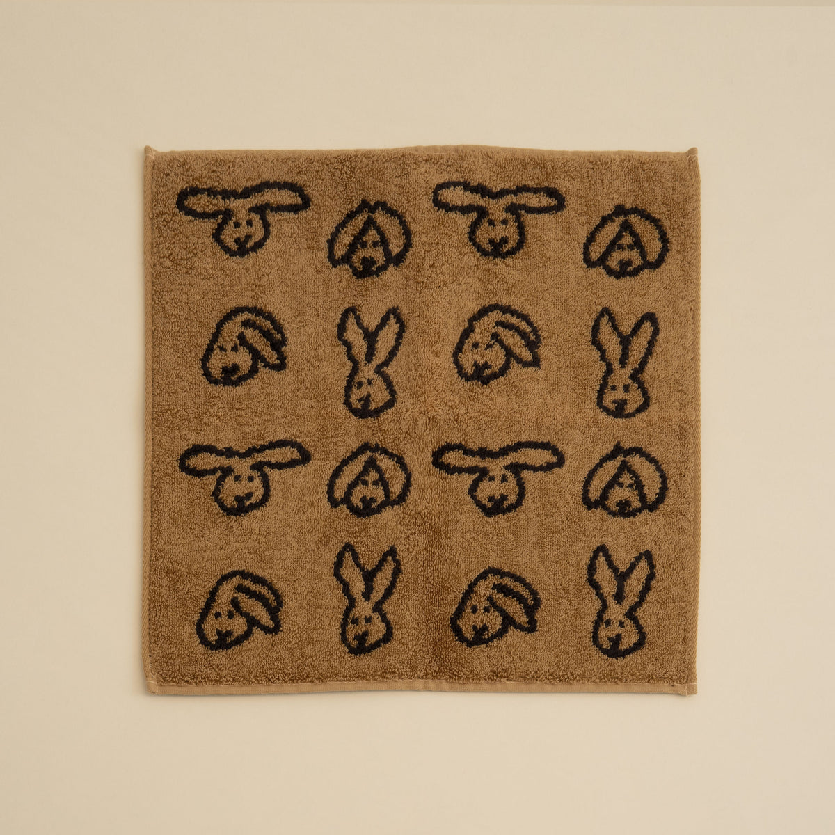 Warmgrey Tail terry face towel with a repeating bunny face pattern on a brown ground