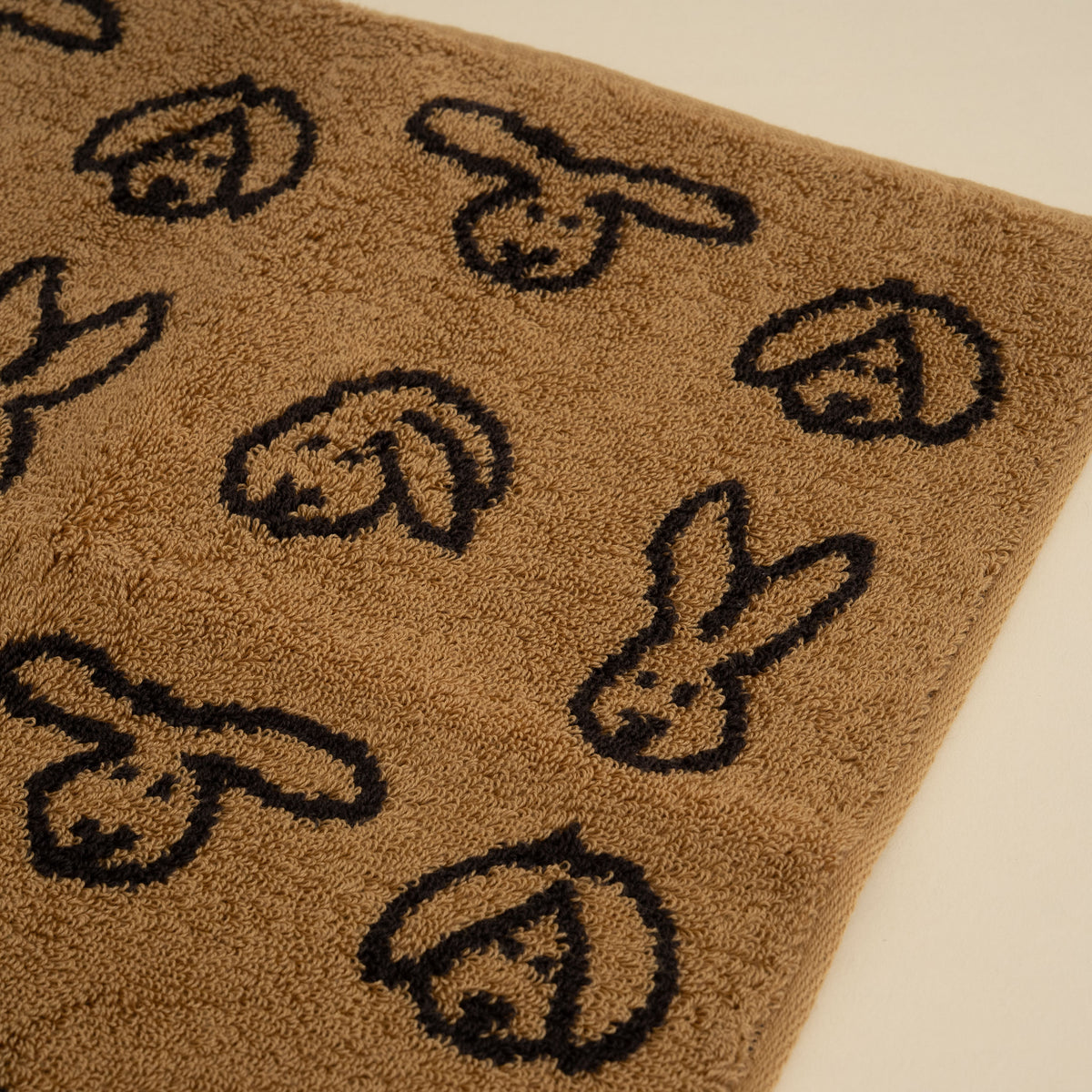 Warmgrey Tail terry face towel with a repeating bunny face pattern on a brown ground