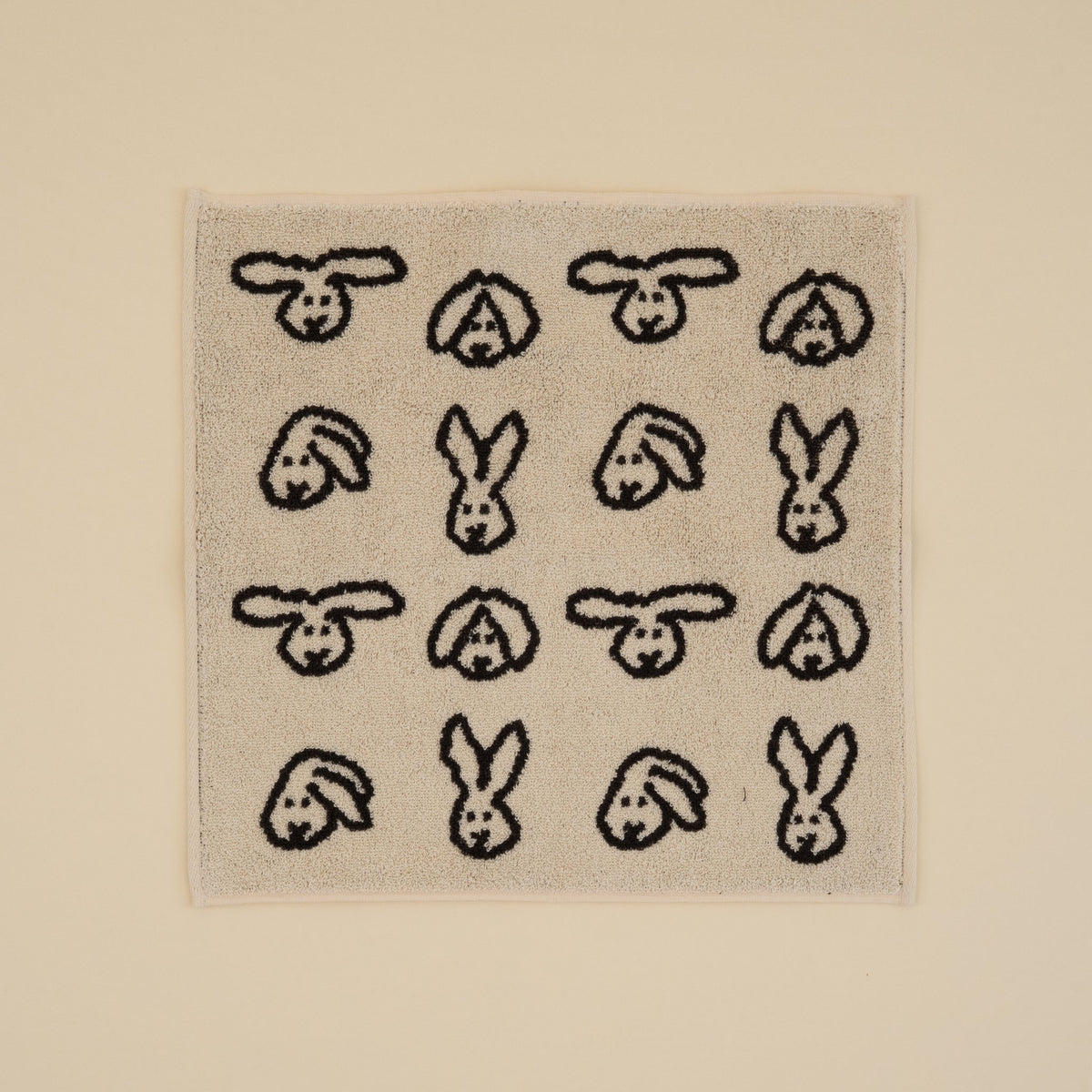 Warmgrey Tail terry face towel with a repeating bunny face pattern on a cream ground