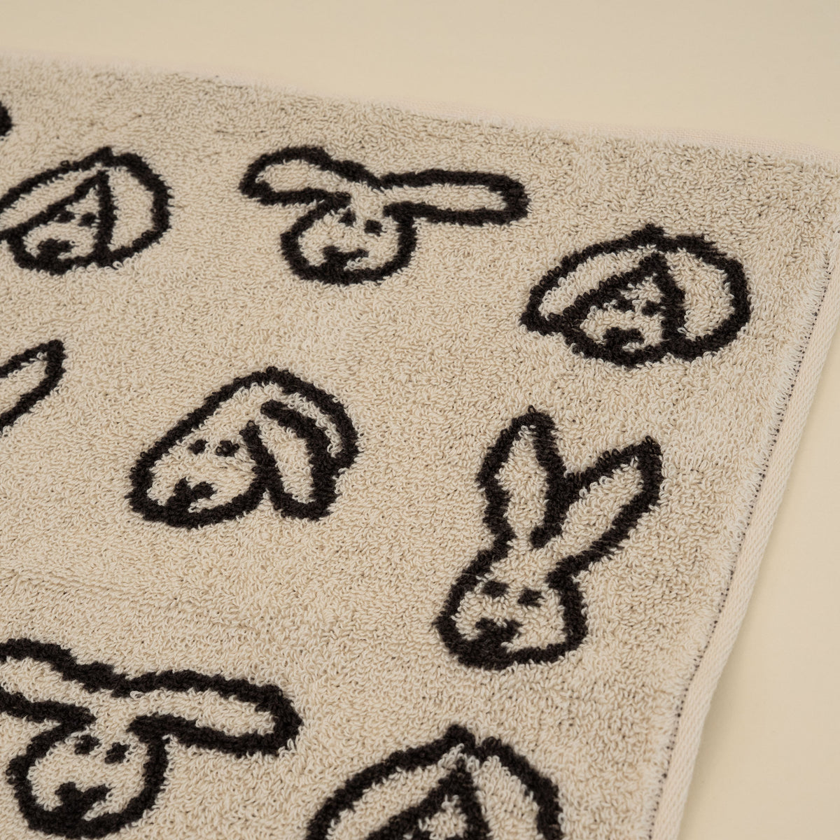 Warmgrey Tail terry face towel with a repeating bunny face pattern on a cream ground
