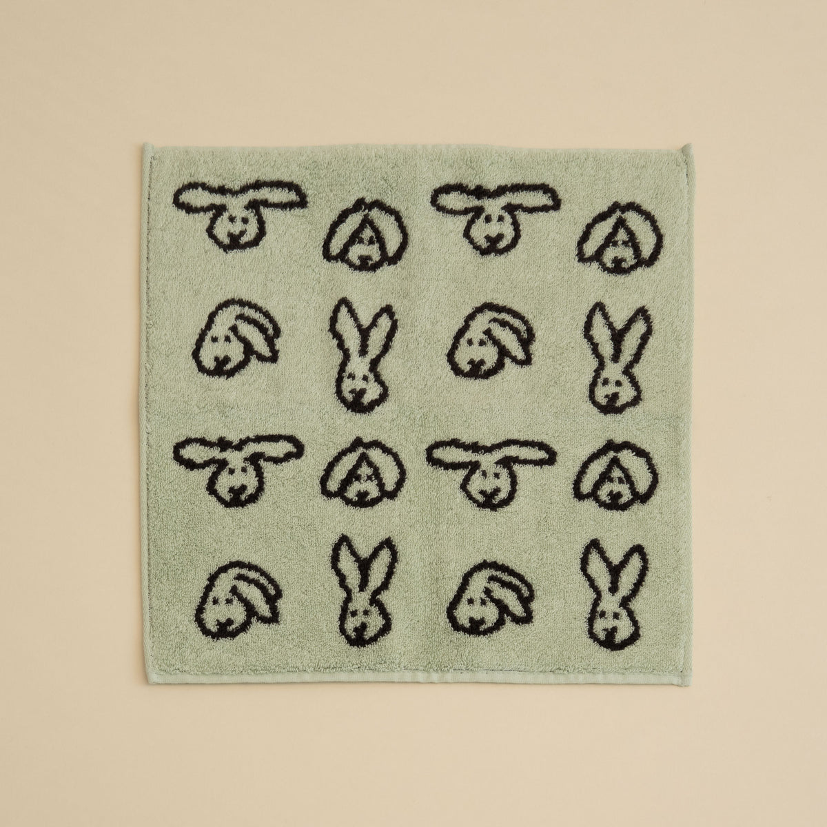Warmgrey Tail terry face towel with a repeating bunny face pattern on a mint ground
