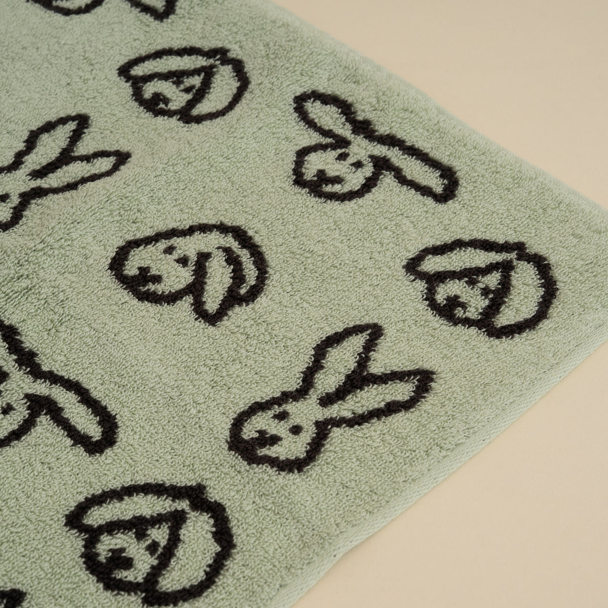 Warmgrey Tail terry face towel with a repeating bunny face pattern on a mint ground