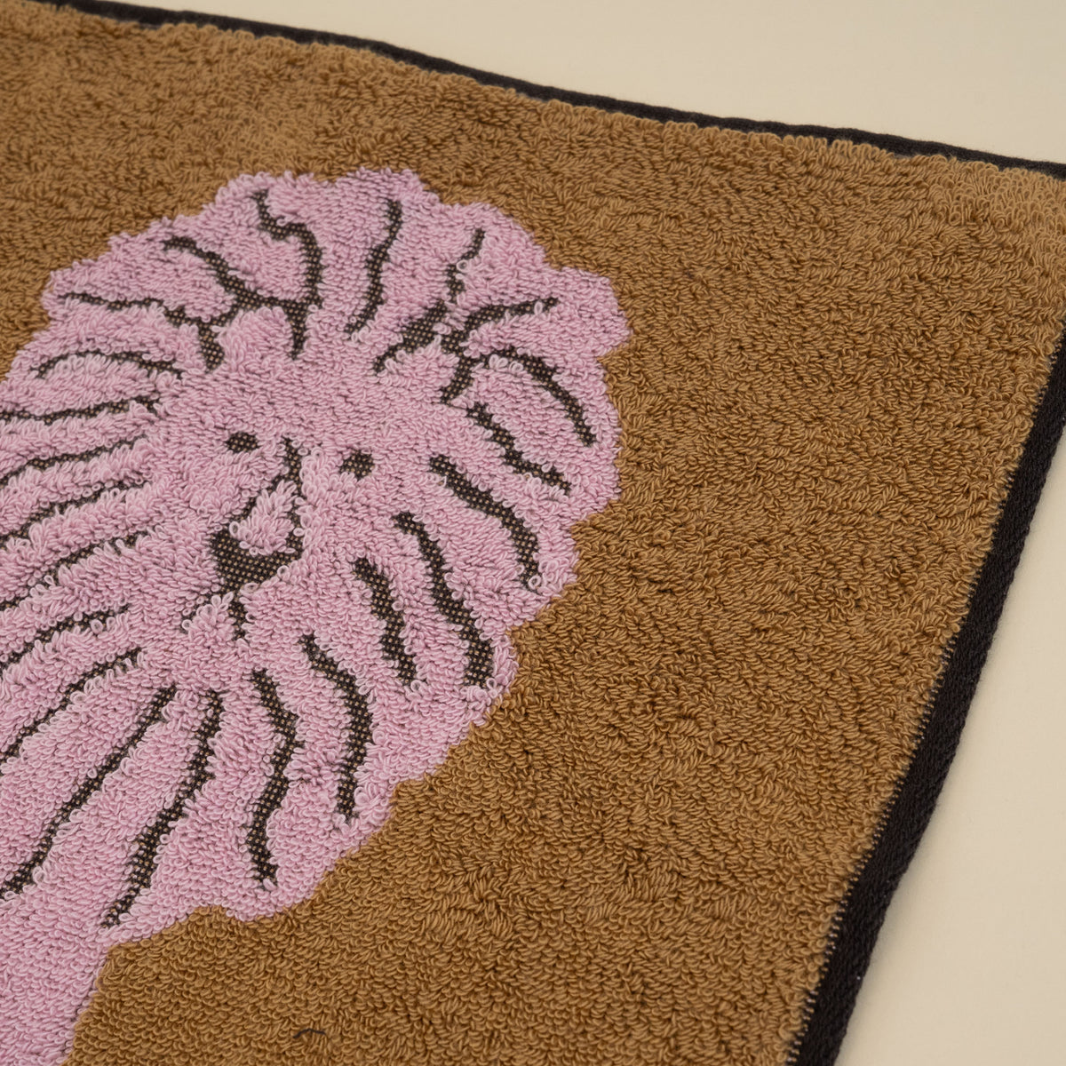 Warmgrey Tail terry face towel with an illustration of a pink lion on a brown ground
