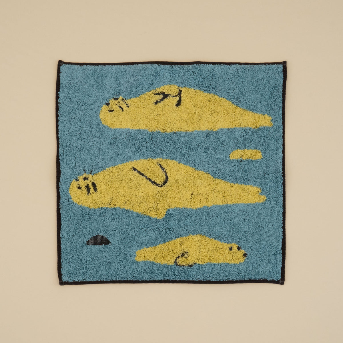 Warmgrey Tail terry face towel with an illustration of yellow seals floating on a blue sea