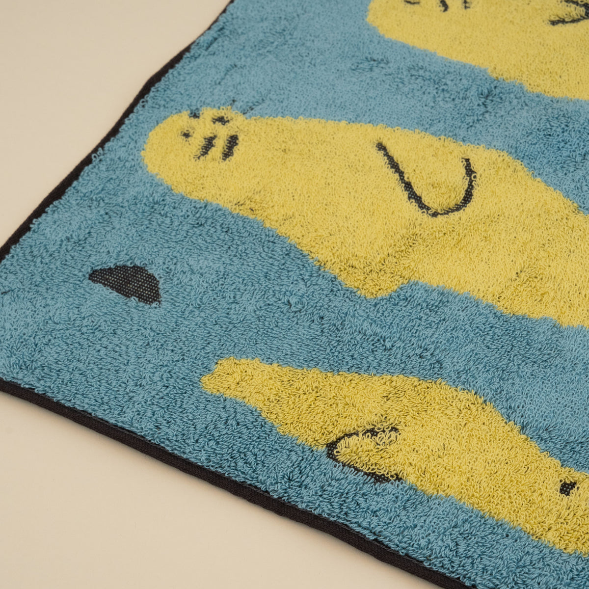 Warmgrey Tail terry face towel with an illustration of yellow seals floating on a blue sea